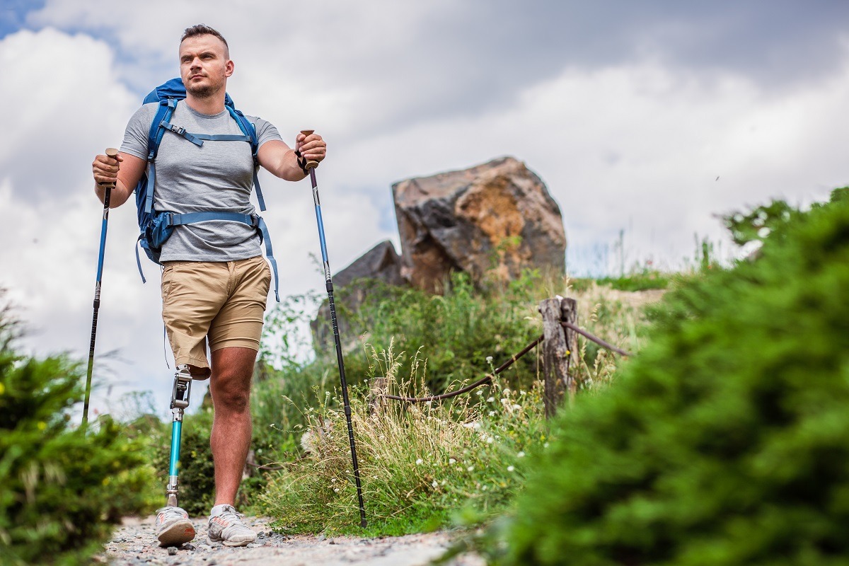 Young confident man with prosthesis trying Nordic walking while spending time outdoors