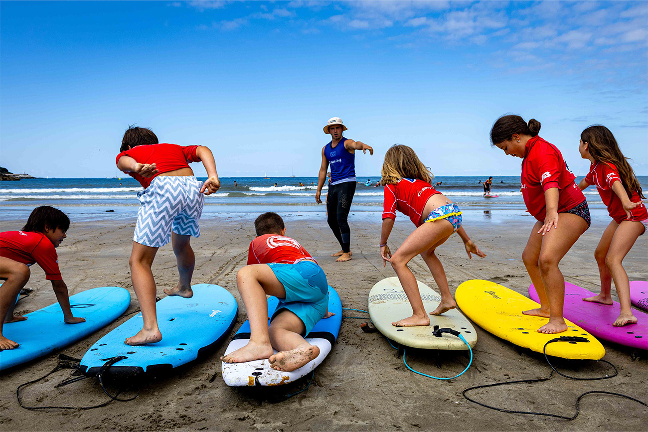 Seis niños y niñas aprenden a surfear en la tabla antes de adentrarse al mar. 