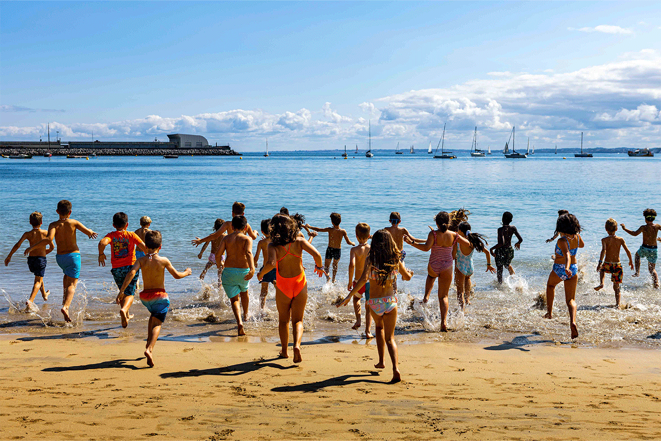 Decenas de niños y niñas corren al agua para disfrutar de un chapuzón. 